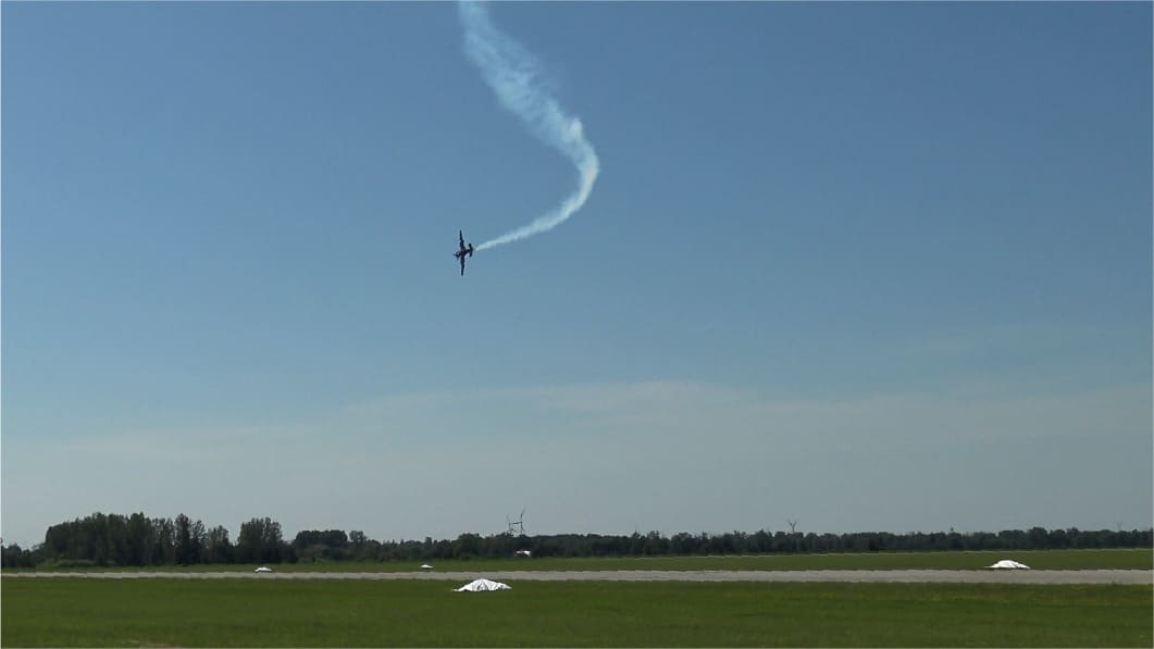A race aircraft trailing smoke through a looping vertical maneuver above the runway