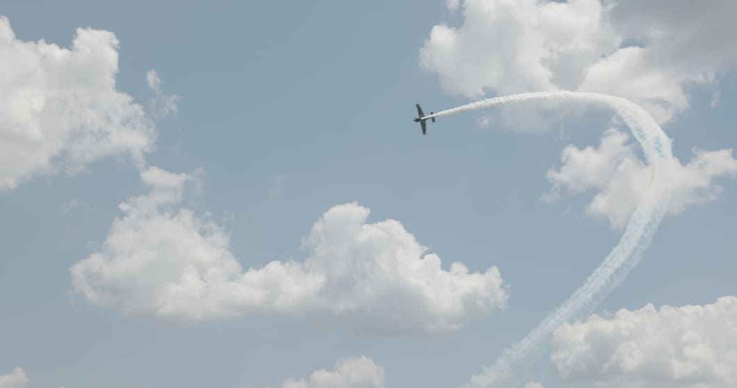 A race aircraft climbing vertically into a looping smoke trail against a cloudy sky